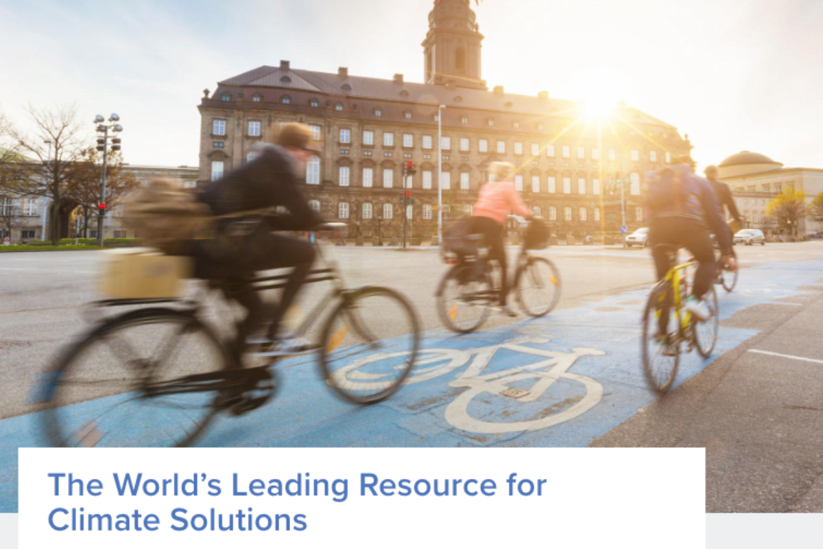 Two cyclists riding in a bike lane with a historic building in the background, representing sustainable transport solutions.